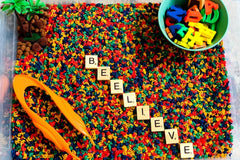 Chicka Chicka Boom Inspired Sensory Bin with primary color dyed alphabet pasta, scrabble letters, rubber letters palm tree and pom poms