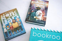 Two children reading books from Bookroo's Tween Book Club subscription on a colorful rug with additional books nearby