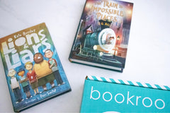 Two children reading books from Bookroo's Tween Book Club subscription on a colorful rug with additional books nearby