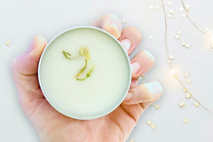 Hand holding the Jas Hands by Greenmade goods showcasing jasmine scented hand salve with dried jasmine buds.