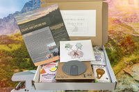 May Escape and Explore box curated with a collapsible cup, drink mixes, tick remover and bug repellant wipes, plus a bonus greeting card. 