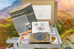 May Escape and Explore box curated with a collapsible cup, drink mixes, tick remover and bug repellant wipes, plus a bonus greeting card. 