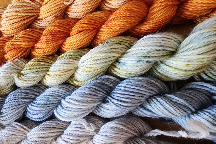 A close up of several skeins of Hand Dyed Baby Alpaca Sport Weight Yarn in Fall colors including grey, blue and orange 