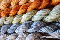 A close up of several skeins of Hand Dyed Baby Alpaca Sport Weight Yarn in Fall colors including grey, blue and orange 
