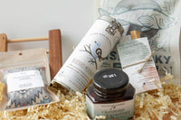 A hand holding a white cap with green text saying "shop small, live well, explore local" for the Explore Local Box monthly subscription
