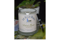 Misty Forest candle with black lid resting on the side of the candle. They are on a stack of French books with potted plants in background