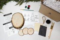 The December 2022 Christmas Crate Club box ingredients laying out on a table - instructions, paint, wood slices, ornaments, etc.
