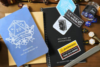 A blue d20 birthday card, a black record of adventure 5e character journal, a glass corked bottle with blue dice, and three other stickers.
