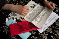 Hands holding various papers and envelopes from the Scarlet Envelope Secret Society escape room subscription box