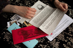 Hands holding various papers and envelopes from the Scarlet Envelope Secret Society escape room subscription box