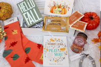 A cozy arrangement of fall-themed items in the Believer's Box VP, featuring socks, a candle, and a faith-inspired book