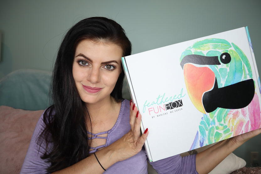 A woman holding up a closed Feathered Fun subscription box.