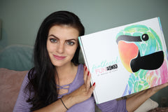 A woman holding up a closed Feathered Fun subscription box.