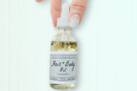 A hand holding the Lavender Hair + Body Oil by Greenmade goods showcasing lavender and jasmine dried botanics inside the bottle.