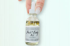 A hand holding the Lavender Hair + Body Oil by Greenmade goods showcasing lavender and jasmine dried botanics inside the bottle.