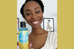 woman with a protective style smiling holding Curls Blueberry Bliss Control Jelly that was used to achieve her hairstyle 