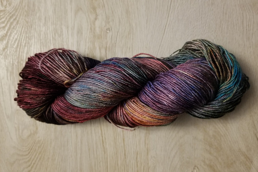 A Skein of Hand Dyed Silk Yarn in Sock Weight that has multiple colors including purple red and black 