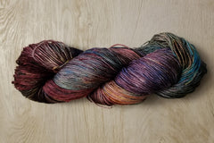 A Skein of Hand Dyed Silk Yarn in Sock Weight that has multiple colors including purple red and black 