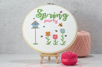 words spring party above colorful flowers with a blue tall birdhouse on this counted cross stitch kit