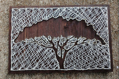 A negative space string art acacia tree. the tree itself is bare wood and the string covers the rest of the board.