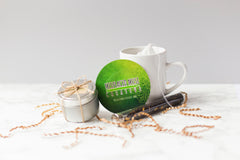A small tin candle is tied in twine like a gift. A round green coaster is propped against a tea mug and a vial of tea.