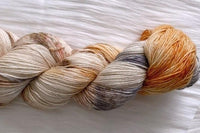 Close up photo of a hand dyed skein of sock weight yarn against a solid background. The skein is twisted and shows a variety of color.