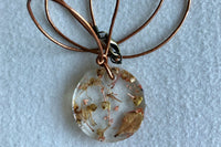 This necklace features an adjustable leather cord and a pendant that was hand made with a preserved flower that was cast in resin.