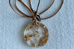 This necklace features an adjustable leather cord and a pendant that was hand made with a preserved flower that was cast in resin.