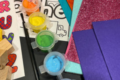 Close-up of Activity Trunk contents featuring paint, pink glitter paper, blue glitter paper, and building blocks
