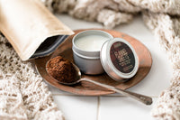 image of travel-sized candle in tin. The lid is off the candle and the label name of "Flannel Sheets" is visible. 