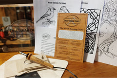 A photo of a custom woodburning tool, a plaque, four coasters, patterns, carbon paper, and the Craftsman Crate box.