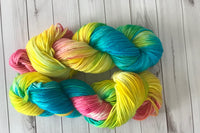 Close up photo of a hand dyed skein of sock weight yarn against a solid background. The skein is twisted and shows a variety of color.