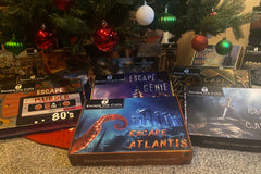 A series of Escape the Crate boxes are below the Christmas tree.  "Escape Atlantis" is in the forefront and past boxes behind it.