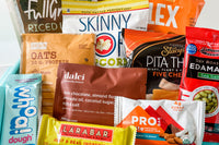 Close up of snacks such as larabar, pita thins, edamame, whoa dough bar, dalci, rx oats, pro bar, skinny pop