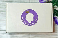 Her Crown and Glory Loc Box subscription on a wooden background with purple flowers in the top right corner of box 