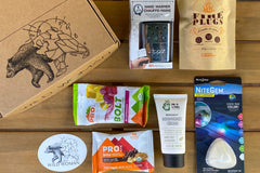 Wild Woman Box subscription boxes stacked on a mountain ledge with a scenic view in the background