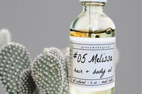 Close up of the Melissa Hair + Body Oil by Greenmade goods showing dried flowers inside the bottle with a cactus in the background.