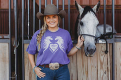 Image showing women wearing one of The Stable Box subscription horse graphic tees standing next to her gray horse. 
