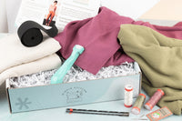 Closeup image of linen fabric in white, purple, and green colorways sitting on top of an open IndieStitch box.