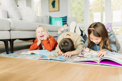 Two children reading books from Bookroo's Tween Book Club subscription on a colorful rug with additional books nearby