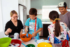 Family baking together using a BāKIT Box kit, mixing ingredients and following a recipe for a fun, hands-on kitchen experience.
