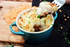 A blue crock filled with shepherd's pie. The lentils in the background suggest that it is a vegetarian recipe.