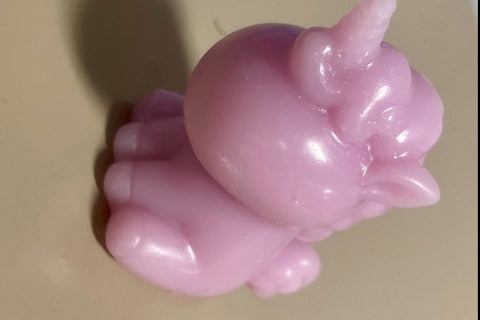A shiny mini soap in a light, almost lilac, purple shaped like a sleeping unicorn sits on a gray base.