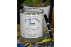 Sea Salt and lily candle with black lid resting on the side of the candle. They are on a stack of French magazines with potted plants behind
