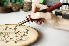 Beginner woodburning tool being held as it burns a Christmas Crate Club project - a gnome wrapped in Christmas lights.