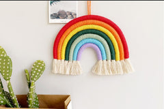 A colorful macrame rainbow wall hanging made of wrapped yarn arches in red, orange, yellow, dark green, light green, blue, and purple.