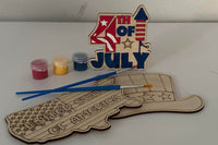 Three wooden patriotic shapes with 2 paint brushes and a paint sampler. One of the shapes is painted as an example.