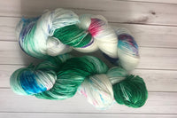 Close up photo of a hand dyed skein of sock weight yarn against a solid background. The skein is twisted and shows a variety of color.