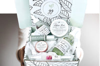 Hands holding a Greenmade goods Beauty Box. Box includes a face serum, lip tin, nail pen, essential oil roller, bath oil, lotion bar.