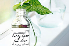 The Buddy System Face Serum by Greenmade goods. Close bottle shot showing a rose bud in the bottle and the clear glass bottle dropper.